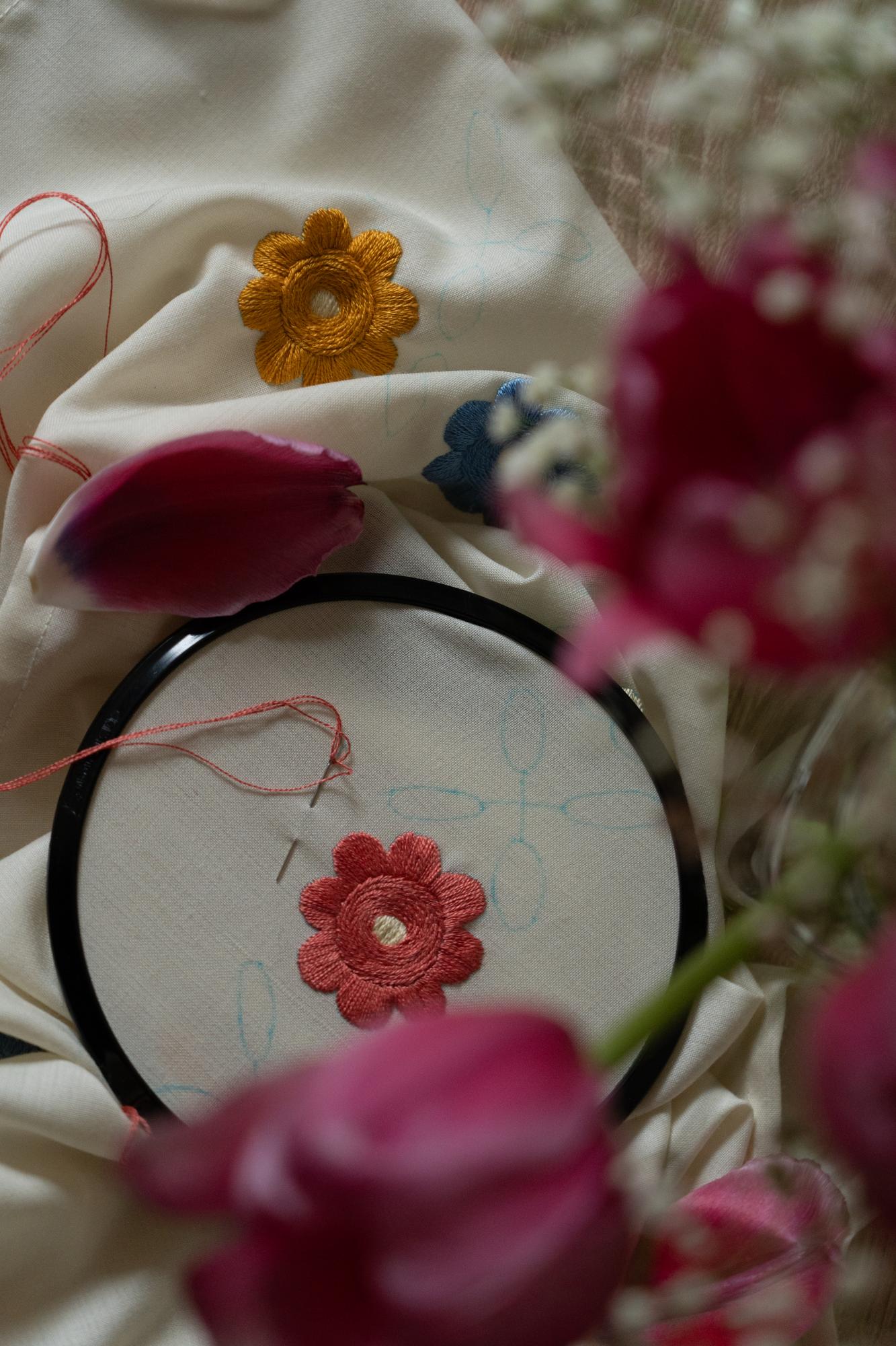 Dettaglio di una mano che ricama un fiore su lino